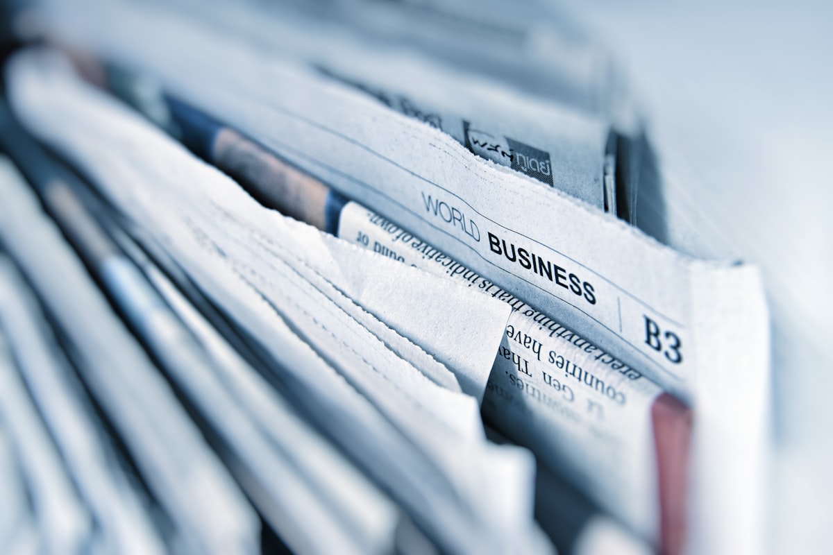 Stack of international newspapers representing the niche and regional publications where policy stories break before reaching national media — often in languages other than English